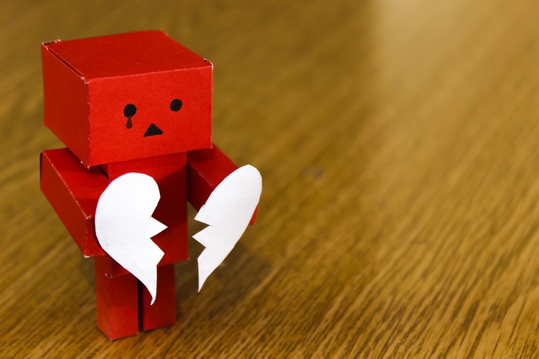 A sad red lego toy holding a teared heart shape paper